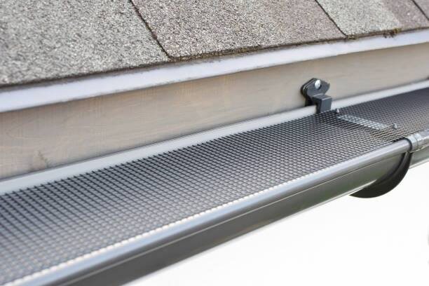 Close-up of a mesh guard seated in a half-round gutter below a shingle roof