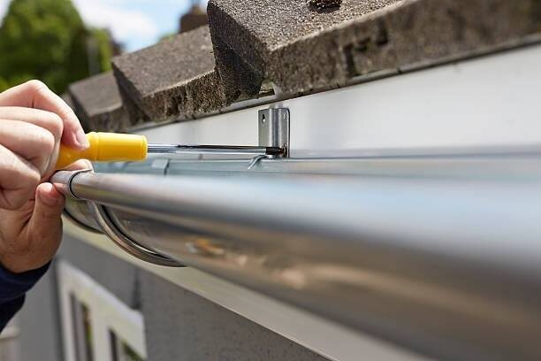 Hand tightening a gutter hanger bracket with a yellow screwdriver
